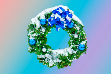 Christmas wreath made of naturalistic looking pine branches decorated with blue balls, ribbon, isolated on pink, turquoise, blue and purple background.の写真素材