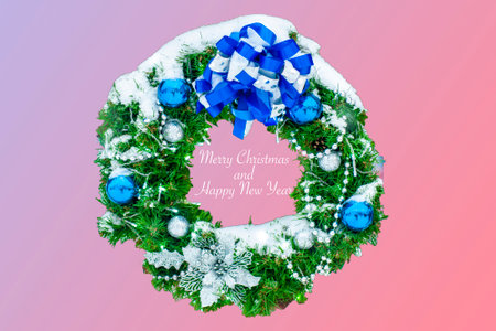 Christmas wreath made of naturalistic looking pine branches decorated with blue balls, ribbon, isolated on pink and purple background. with the inscription text : "Merry Christmas and Happy New Year"の写真素材