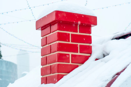 Red smoke brick pipe, chimney close-up, on the roof of a snow-covered house. Symbol of the New Year holidays, Christmas and the arrival of Santa Claus. Snowdrifts on the roof with a chimney.の写真素材