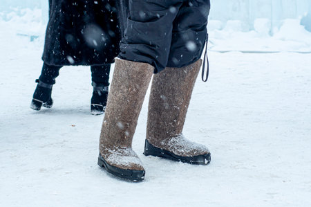 Winter footwear felt boots - close-up. A man stands in the winter on the street, in the snow in felt boots. Warm felt boots made of animal hair. traditional shoes. Symbol of cold, frost.の写真素材