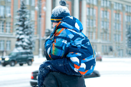 The little boy, son sits on his strong shoulders of his father, outdoors in winter. Child with dad on New Year's holidays. A boy in warm winter clothes is walking with his father for a walkの写真素材