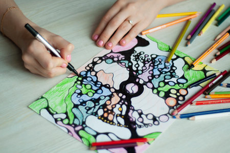 Close-up of female hands drawing neurographic art. Mental health, adult fine motor skills, creativity, psychology. Abstract neurographic drawing with a marker, colored pencils. Art. selective focus.の写真素材