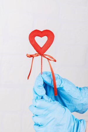 Female hand in blue medical gloves holding a red heart, symbol of life. Concept support of people infected of coronavirus, protect and difend the world and eath from covid-19, space for textの写真素材