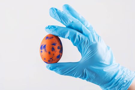 Easter time in quarantine concept. Female hand in blue medical gloves holding Easter egg. Concept of Easter holyday and spring break during epidemy of coronavirus, protect the world from covid-19の写真素材