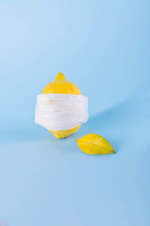 Ill lemon in a face protective mask on a blue pastel background, protection against coronavirus, viruses and infections, minimal immunity protection concept, space for textの写真素材