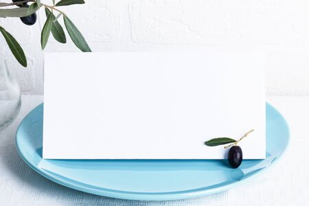Minimalistic wedding composition with empty cards mock up for invitation, menu, place card on a pastel blue porcelain plate with olive branch on white background. top view stylish art conceptの写真素材