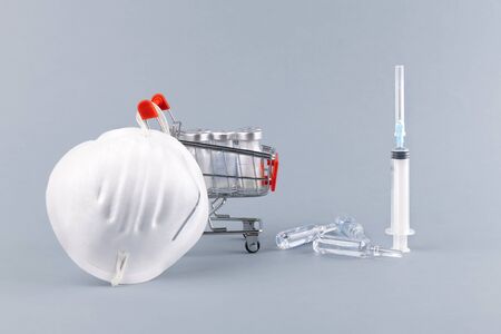 Coronavirus protection concept. Mini grocery cart with medicines, syringe and medical face shield. Protect Yourself from coronavirus. Protection against pollution, virus, flu and infectionの写真素材