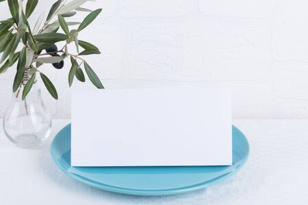Minimalistic wedding composition with empty cards mock up for invitation, menu, place card on a pastel blue porcelain plate with olive branch on white background. top view stylish art conceptの写真素材
