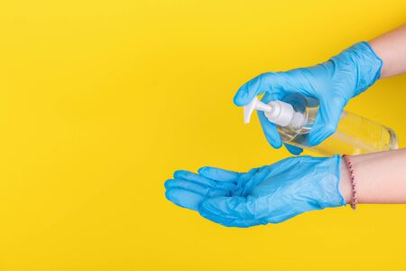 Female hand in latex surgical gloves is using antiseptic hand sanitizer, yellow background. Alcohol based sanitizer gel for hand hygiene protect from coronavirus covid-19, copy spaceの写真素材