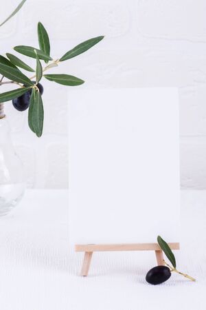 Festive wedding, birthday or business table setting and mock up invitation with olive branch on white background. Blank card mockup. Minimal home decor. Simple modern interior designの写真素材