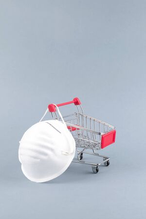 Coronavirus protection concept. Mini grocery cart and medical face shield. Protect Yourself with mask from coronavirus while shopping, space for textの写真素材