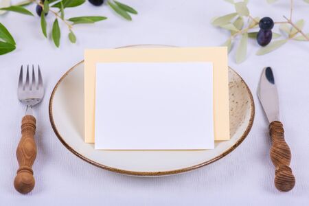 Minimalistic wedding composition with empty cards mock up for invitation, menu, place card with olive branch on white background. Cozy festive fall table setting. Minimal restaurant menu concept.の写真素材