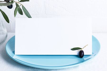 Minimalistic wedding composition with empty cards mock up for invitation, menu, place card on a pastel blue porcelain plate with olive branch on white background. top view stylish art conceptの写真素材