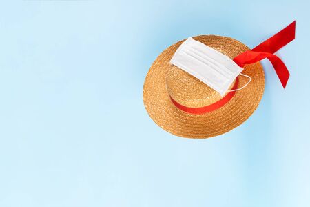 A straw hat is wearing a protective medical mask and is flying down on a blue pastel background. Coronavirus summer vacation, Covid-19 and travel concept. Health protection during the tripの写真素材