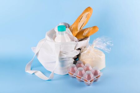 Basic essential food products, milk, bread, flour, eggs in an eco-cotton bag, safe food delivery concept and volunteer during coronavirus covid-19, social assistance conceptの写真素材