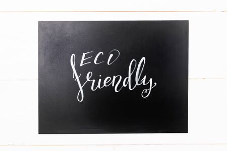 white lettering eco friendly , message on a black chalkboard on a white wooden backgroundの写真素材
