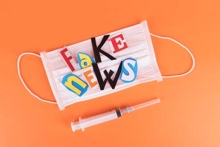 L'insciption Fake news, collage of colored paper's letters, medical face mask and syringe on a orange background, concept of lies in social networks during world coronavirus pandemicの写真素材