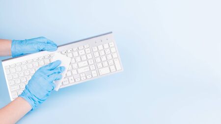Female hands with blue medical gloves are cleaning a keyboard with disinfectant for prevention the spread of coronavirus. Woman is using alcohol based gel for protection from covid-19, copy spaceの写真素材