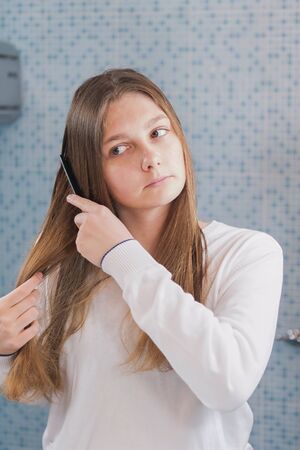 A beautiful girl is combing her hair herself, looking in mirror in the bathroom, morning routine, selective focusの写真素材