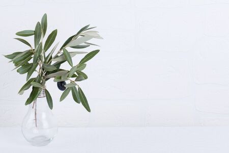green olive branches in light bulb glass vase on a white brick wall background. Wall mockup. Minimal home decor. Fall Interior design. Copy spaceの写真素材