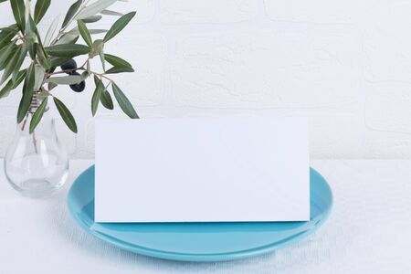 Minimalistic wedding composition with empty cards mock up for invitation, menu, place card on a pastel blue porcelain plate with olive branch on white background. top view stylish art conceptの写真素材