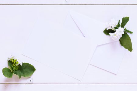Blank white greeting card with white envelope and white flowers with on a wooden white table. Valentine and love concept, wedding invitationの写真素材