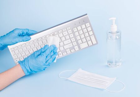 Female hands with blue medical gloves are cleaning a keyboard with disinfectant for prevention the spread of coronavirus. Woman is using alcohol based gel for protection from covid-19, copy spaceの写真素材