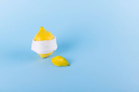 Ill lemon in a face protective mask on a blue pastel background, protection against coronavirus, viruses and infections, minimal immunity protection concept, space for textの写真素材