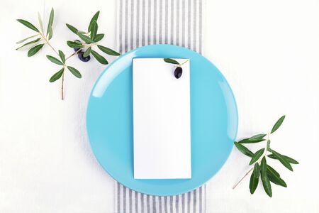 Festive wedding, birthday table setting with golden cutlery, olive branch, pastel blue porcelain plate. Blank card mockup. Minimal restaurant menu concept. Flat lay, top viewの写真素材