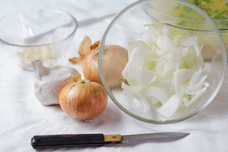 fresh sliced onions with a glass bowl close-up and a whole onion and garlic on a light background, cooking, selective focusの写真素材