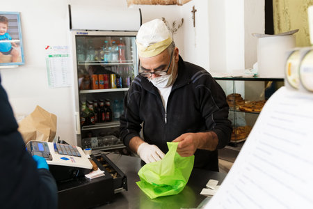 Avetrana, Italy, - Marth, 13, 2020. An Italian baker wearing medical face mask respecting health...