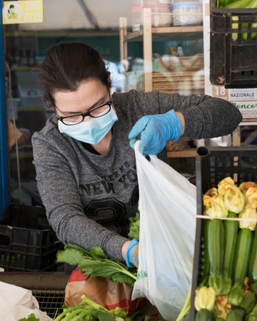 Avetrana, Italy, - Marth, 13, 2020. An Italian greengrocer serving a costumer wearing medical mask...