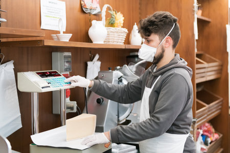 Avetrana, Italy, - Marth 19, 2020. Salesman is serving a costumer a cheese, wearing medical mask and gloves protection during Coronavirus epidemy. Shopping, pandemia of Covid-19, quarantineのeditorial素材