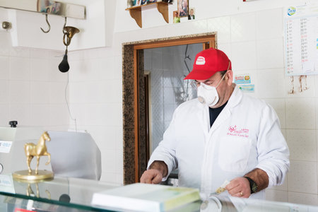 Avetrana, Italy, - Marth 19, 2020. Salesman is serving a costumer a meat, wearing medical mask and gloves protection during Coronavirus epidemy. Shopping, pandemia of Covid-19, quarantineのeditorial素材