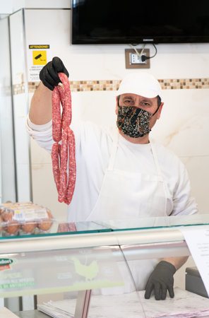 Avetrana, Italy, - Marth 21, 2020. Salesman is serving a costumer a meat, wearing handemade mask and gloves protection during Coronavirus epidemy. Shopping, pandemia of Covid-19, quarantineのeditorial素材