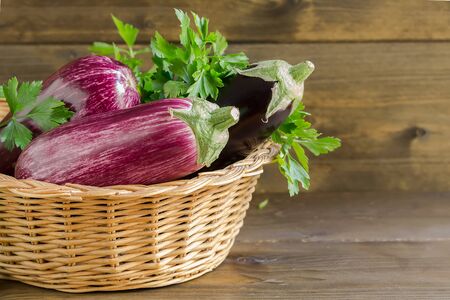 Fresh raw Purple Eggplant in a wicker basket on wooden background, copy spaceの写真素材