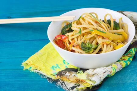Asia food. Stir fry udon noodles with vegetables on a blue wooden backgound, cooked in wokの写真素材