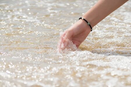 Female hand touches the sea water at the shore. The concept of summer and holidays.の写真素材