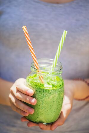 Summer healthy detox drink: blended green smoothie in the bright midday sun, in the hands of a young girl, selective focus. Healthy eating conceptの写真素材