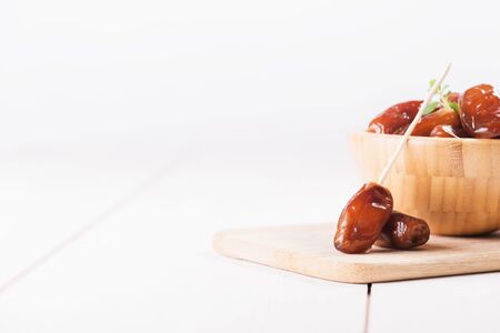Close up of a date on a stick. Raw sweet dry dates with in a wooden bowl on a white background....