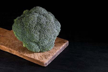 Fresh broccoli on a cutting board on a black background, rustic style, dark key. Healthy food. Copy spaceの写真素材