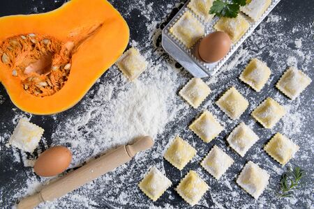 Fresh pumpkin and cottage cheese ravioli with flour on a dark background. Process of making italian ravioli. Horizontal top view with copy spaceの写真素材