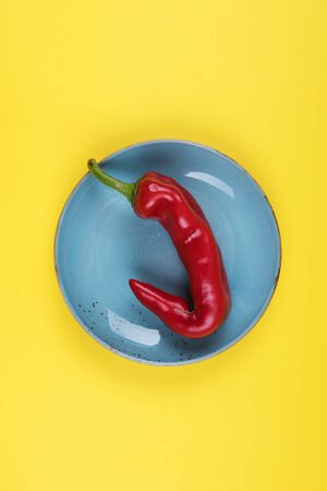 Trendy ugly red chili peppers on a blue plate on a yellow background, minimal style of nature, pop art, creative food concept, modern artの写真素材