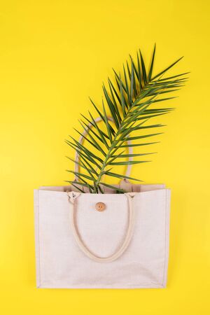Eco friendly cotton bag with palm leaf on a yellow background, copy space, minimal nature style. Environmental Conservation Recycling Concept, zero waste and plastic freeの写真素材