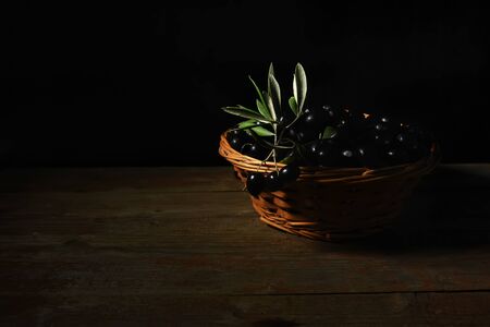 Close up of a wicker basket full with black olives from Puglia, Italy over a wooden table on a black background. Fresh harvest of traditional products of Salento, Italy, copy spaceの写真素材