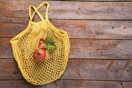 Autumn ecology flat lay: yellow mesh or net bag of cotton with one red apples and one fall leaf on old rustic wooden boards. Top view background with copy spaceの写真素材