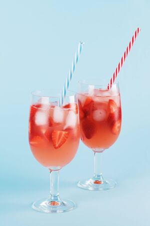 Fresh summer cocktail with strawberry and ice cubes. Two glasses with strawberry, ice and wine, strawberry sangria on a pastel blue backgound, minimalism, minimalism, copy spaceの写真素材