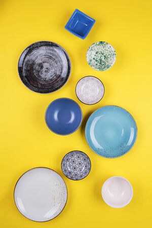 Set of colorful modern porcelain plates and bowls on a yellow background. designer ceramic bowls in different colors stacked together. Blue, turquoise, grey and dark blue bowls. Top viewの写真素材