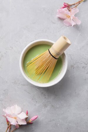 Top view of green tea matcha with bamboo chasen in a bowl on gray marble with beautiful oleander...