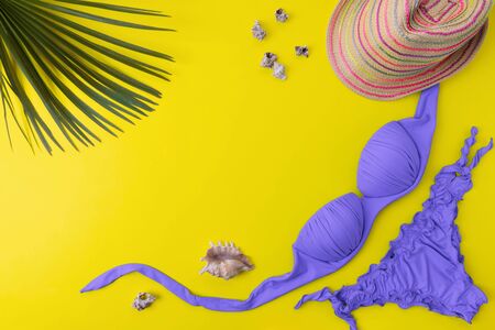 Bikini swimsuit with tropical palm's leaves on a yellow background. Overhead view of woman's swimwear and beach accessories with copy spaceの写真素材